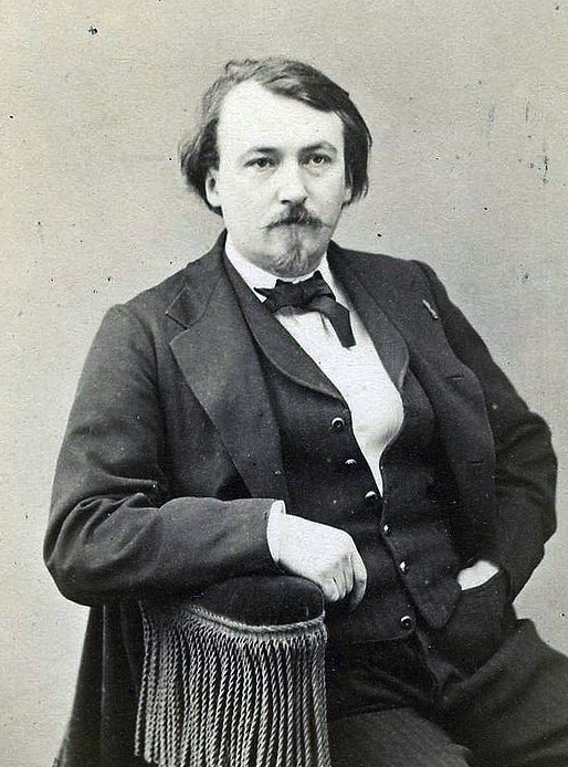 A formal black and white portrait of a mustachioed man sitting in a chair, dressed in a suit with a bow tie.
