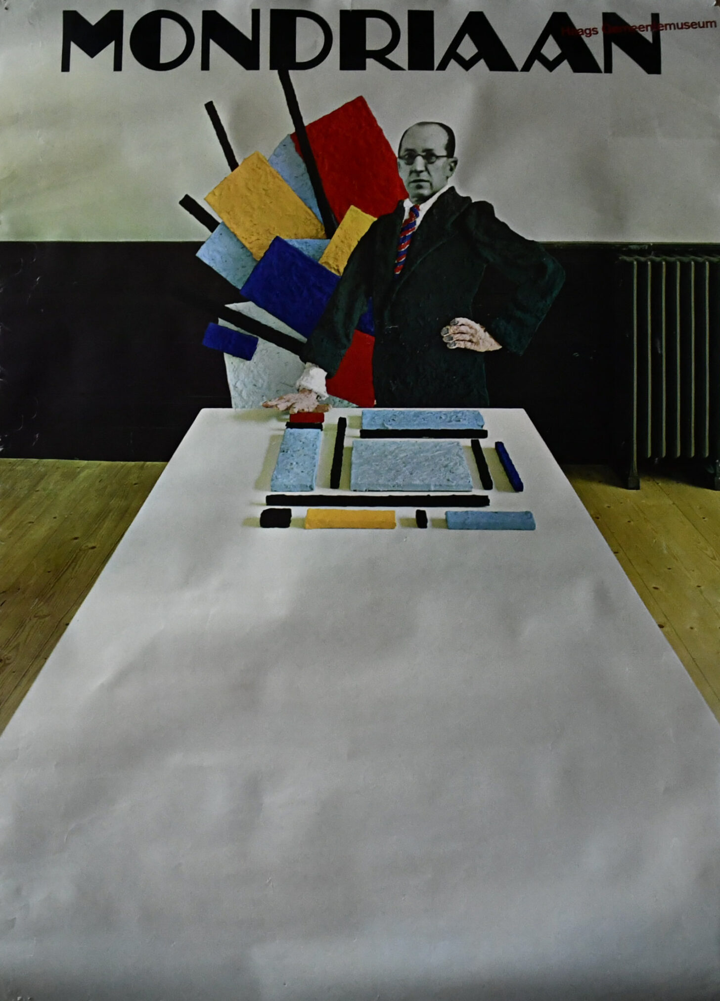 A vintage poster featuring a stylized depiction of Piet Mondrian standing beside a table displaying colored geometric shapes and blocks, with vibrant colors and abstract elements in the background.