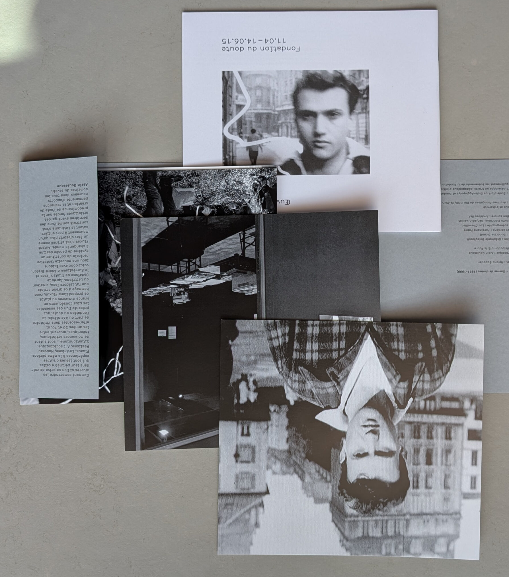 A flat lay of several printed materials, including photographs and text pages related to Isidore Isou and the Lettrism movement, with a prominent upside-down black and white photo of a young man in a plaid shirt.