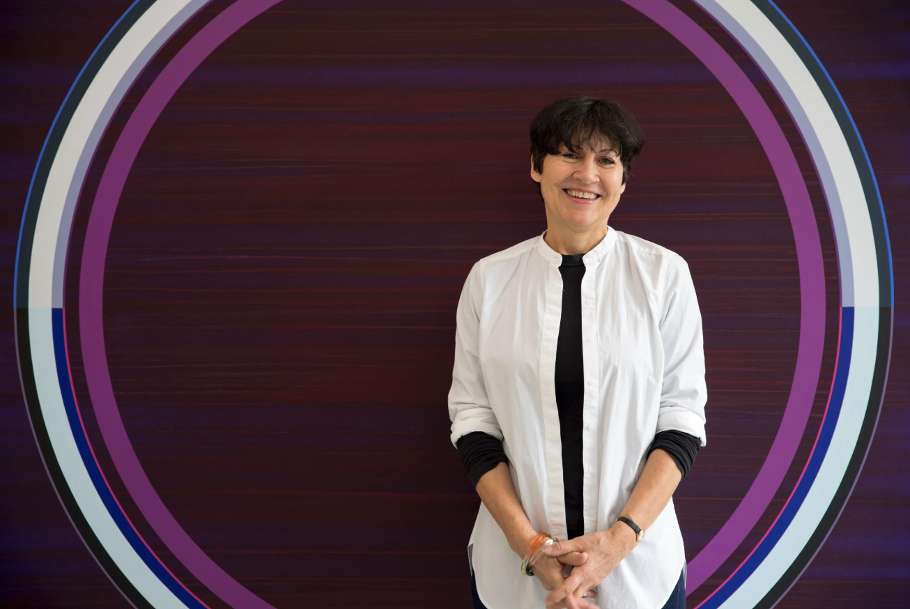 A smiling artist stands in front of a large abstract artwork featuring concentric circles in various colors against a deep purple background.