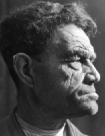 A black and white side profile portrait of an older man with curly hair and deep facial wrinkles, looking intently into the distance.