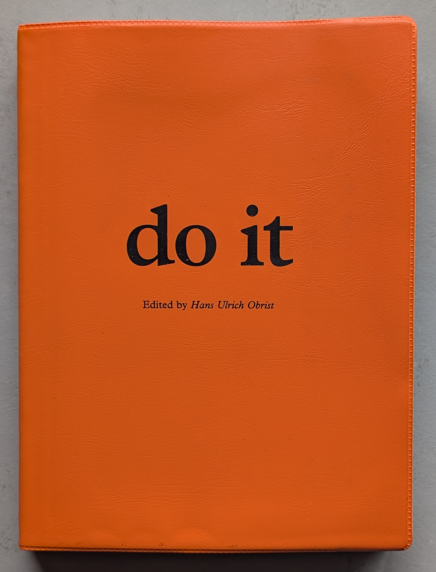 Cover of the book 'do it', edited by Hans Ulrich Obrist, featuring an orange background and bold black text.