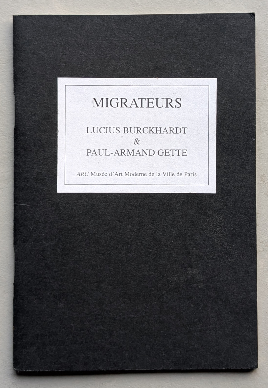 Cover of the publication 'MIGRATEURS' by Lucius Burckhardt and Paul-Armand Gette, featuring a black background with a white label containing the title and authors' names.